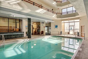 Ein Hallenbad mit klarem Wasser, einem Sprungbrett und Blick durch große Fenster nach draußen.