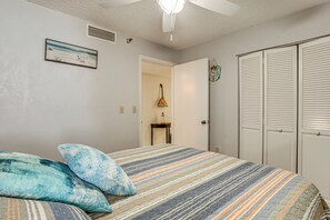 A bedroom with a bed, pillows, a nightstand, a lamp, a closet, and a door leading to another room. - Dream Daytona Getaway: Beachfront Condo! (Daytona Beach)