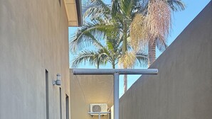 A narrow outdoor corridor with a grassy area, a white pole, and a wall-mounted air conditioning unit. - Flat near American international school (Lusaka)