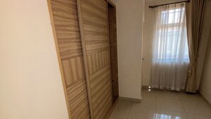 A room with a tiled floor, a wooden wardrobe, a window with curtains, and a staircase with a handrail. - Flat near American international school (Lusaka)