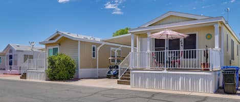 A row of mobile homes with a covered porch and a small garden area.