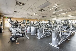 Ein Fitnessraum mit mehreren Cardiogeräten, einem Deckenventilator und einer Tür mit der Aufschrift 'EXIT'.