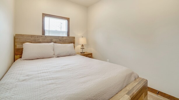 Una cama bien hecha con cabecera de madera, una lámpara de noche y una ventana con persianas.
