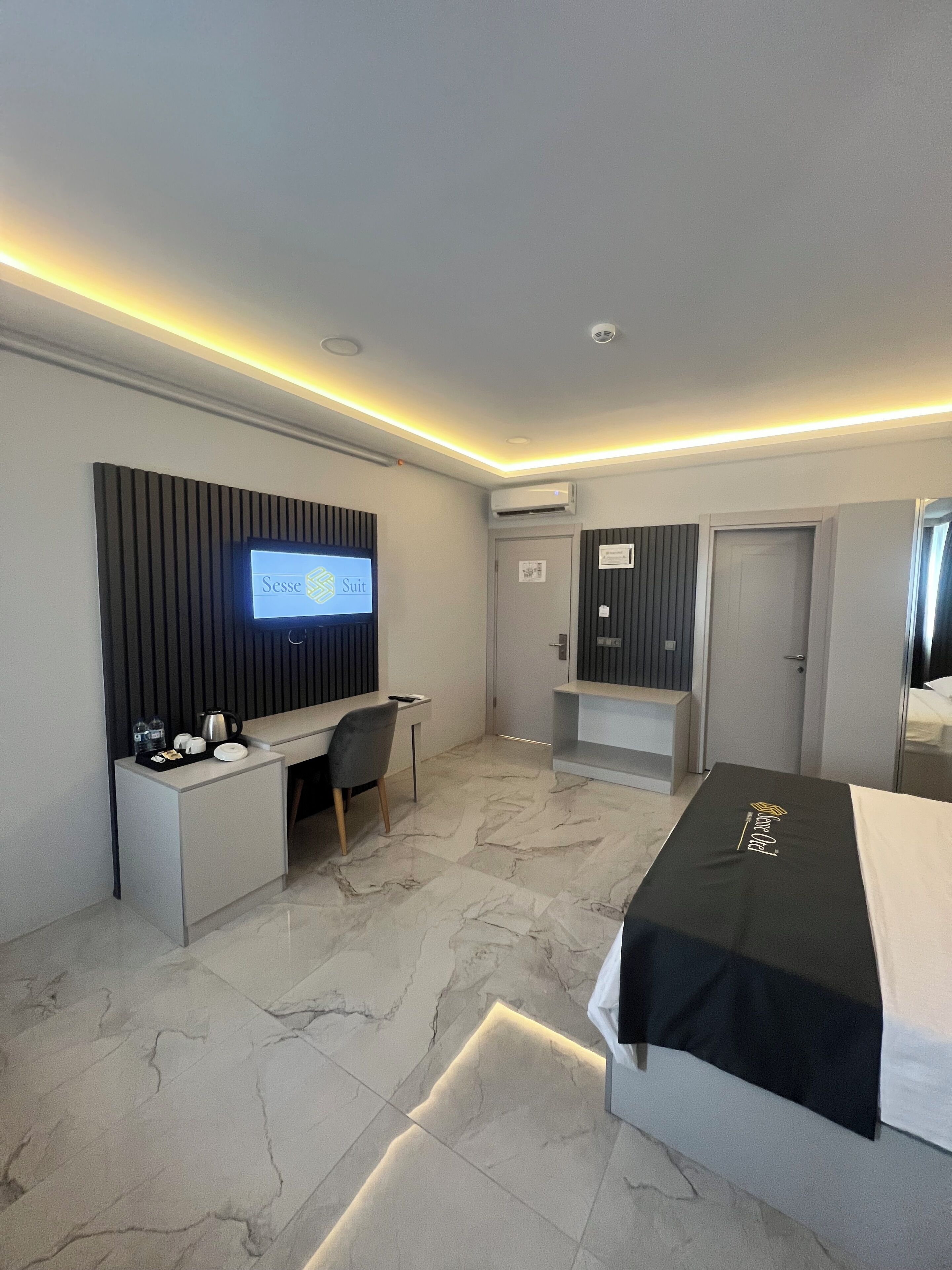 Una habitación de hotel moderna con televisión de pantalla plana, un escritorio con silla, una cama y un armario.