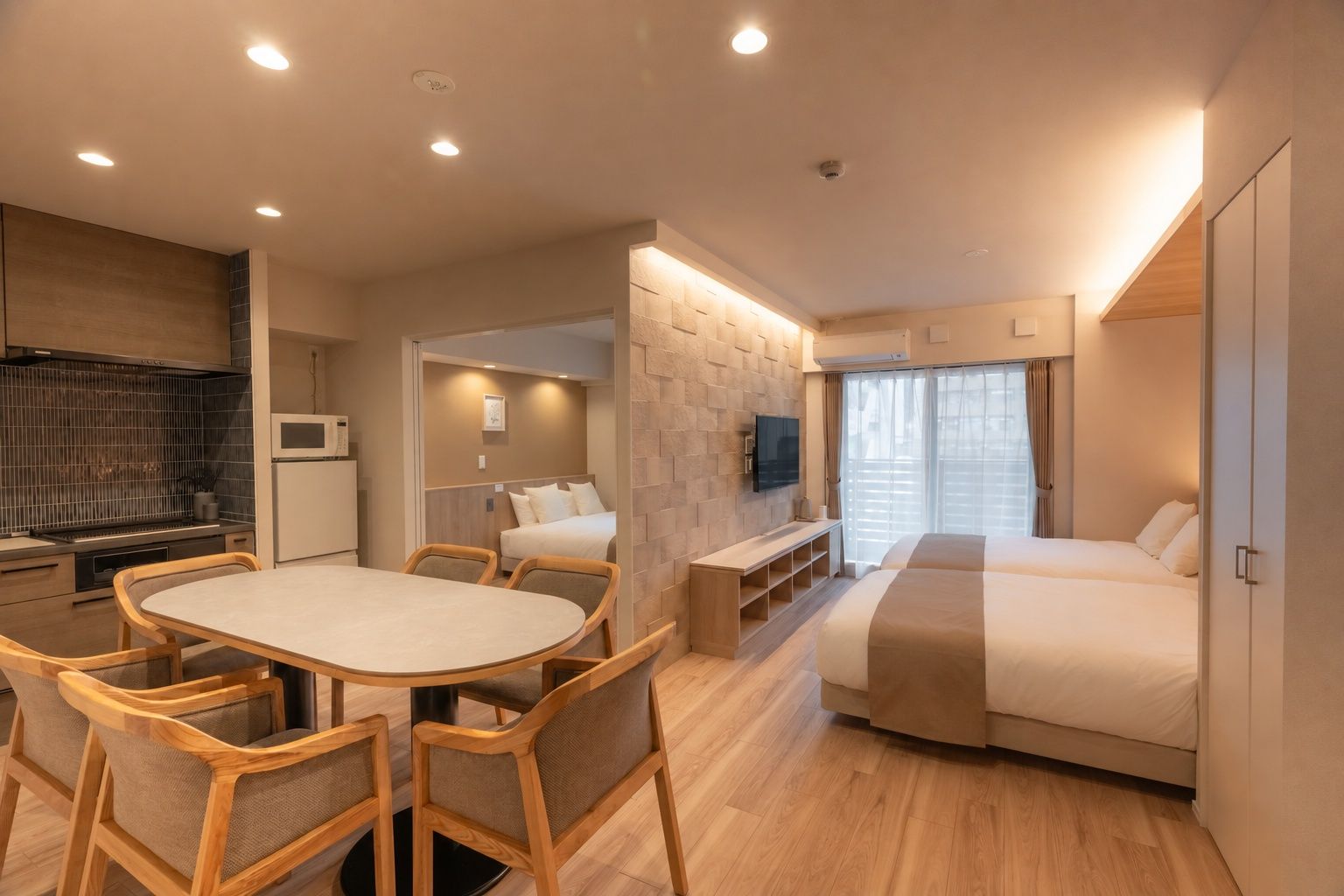 Une chambre d’hôtel compacte comprenant un coin cuisine, un espace repas avec une table et des chaises, un lit et un téléviseur.