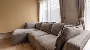Un canapé modulable au design incurvé, placé contre un mur beige agrémenté d’une fenêtre et de rideaux.