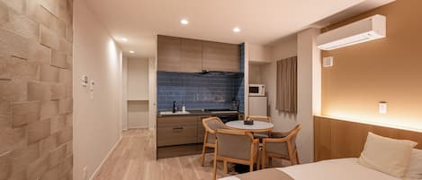 Quarto de hotel com cama, pequena área de refeições com mesa e cadeiras, cozinha compacta e ar condicionado instalado.
