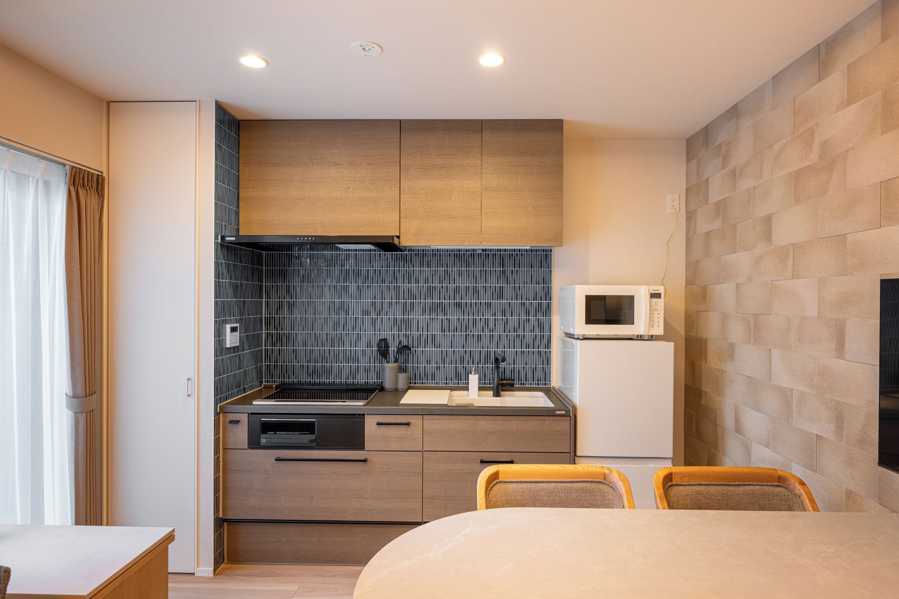 A compact hotel room with a kitchenette, a bed, and a seating area.