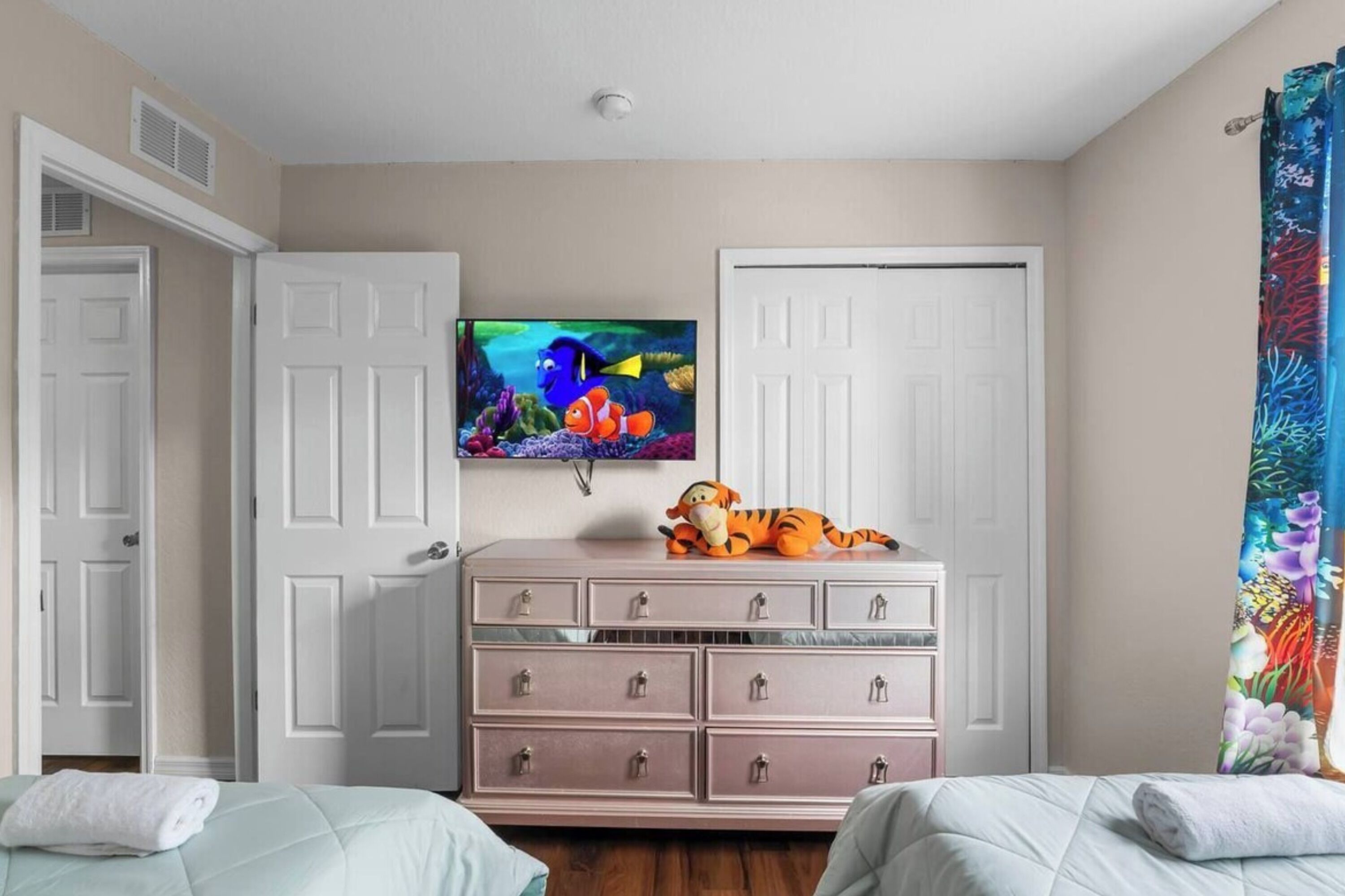 Un dormitorio con dos camas, un aparador, un televisor en la pared y una puerta.