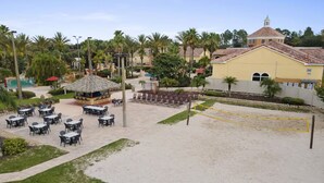 Un espace aménagé au bord de la plage, avec des sièges en plein air, un filet de volley-ball et un bâtiment doté d’un toit rouge.
