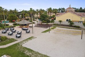 A beachside area with outdoor seating, a volleyball net, and a building with a red roof. - Spacious 4/3 Townhome in Regal Palms Resort (Davenport)
