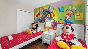 Une chambre d’enfant avec deux lits simples, une fresque murale colorée et des peluches à l’effigie de Mickey Mouse.