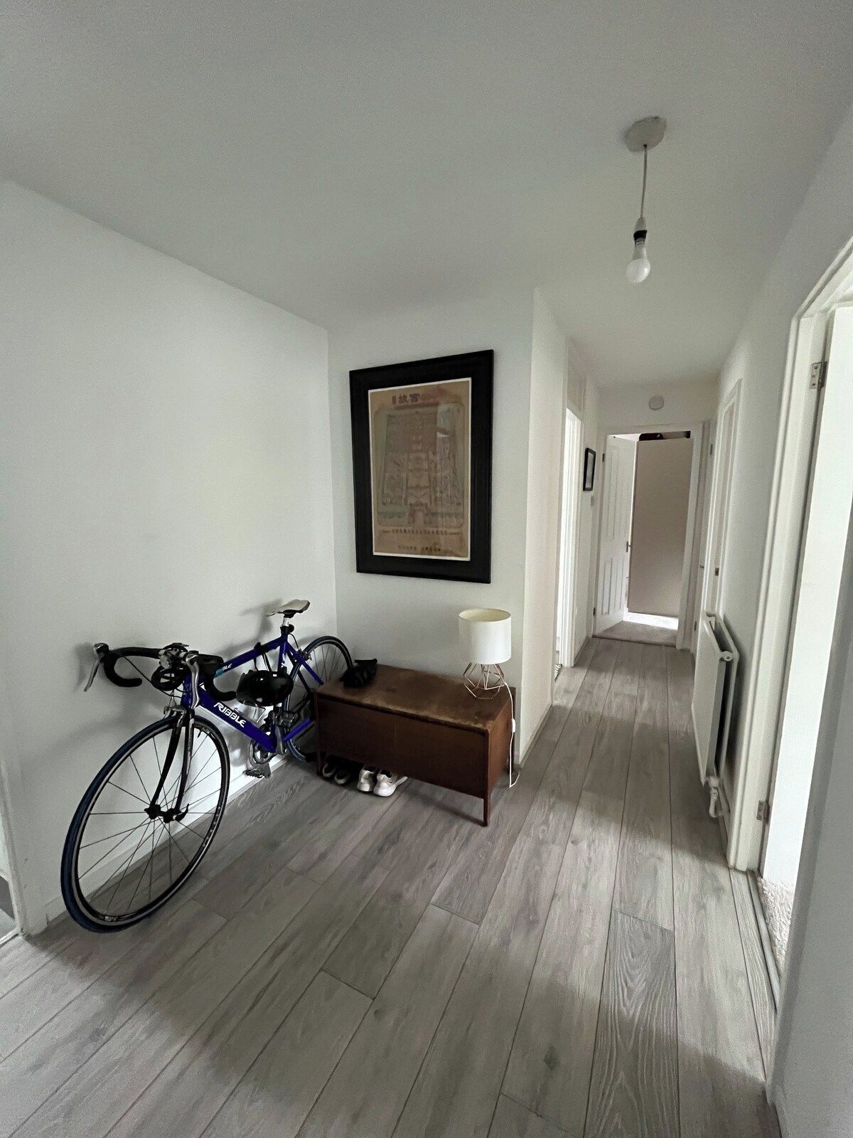 A hallway with a bicycle leaning against the wall, a framed picture on the wall, and a bench with a lamp.
