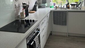 Uma cozinha moderna com fogão embutido, armários brancos e janela com vista para o verde lá fora.