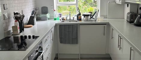 Una cocina moderna con armarios blancos, horno empotrado y ventana con vistas a zonas verdes.