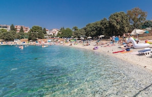 A beach with clear water, umbrellas, and people sunbathing.