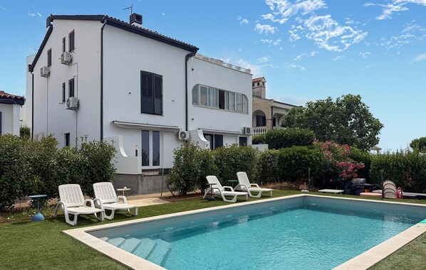A two-story building with a swimming pool, outdoor seating, and a well-maintained garden.
