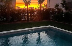 A swimming pool with a sunset view, surrounded by palm trees and a grassy area. - 1 bedroom stunning apartment in Pula (Pula)