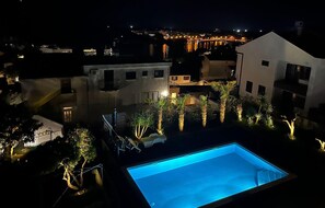A nighttime view of a residential area with a swimming pool, palm trees, and buildings with illuminated windows. - Cozy apartment in Pula with outdoor swimming pool (Pula)