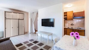 Een moderne kamer met een televisie, een eettafel met bloemen, een bankje en een kitchenette.