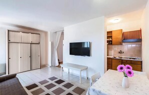 A modern room with a TV, a dining table with flowers, a bench, and a kitchenette. - Cozy apartment in Pula with outdoor swimming pool (Pula)