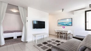 Een moderne woonkamer met een flatscreen televisie, een eethoek met een tafel en stoelen, een bank en een kamerbreed tapijt.