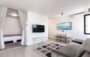 A modern living room with a flat-screen TV, a dining area with a table and chairs, a sofa, and a patterned rug. - Cozy apartment in Pula with outdoor swimming pool (Pula)