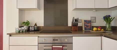 A modern kitchen with a built-in oven, a range hood, and a sink. There are various kitchen utensils and a book on the counter.