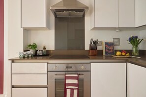 A modern kitchen with a built-in oven, a range hood, and a sink. There are various kitchen utensils and a book on the counter. - Entire 2 bed, 2 bath near Canning Town & River (Greater London)