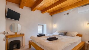 Een slaapkamer met een houten bed, een nachtkastje, een spiegel, een wandtelevisie en een raam.