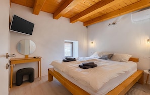 Ein Schlafzimmer mit einem hölzernen Bett, einem Nachttisch, einem Spiegel, einem an der Wand montierten Fernseher und einem Fenster.