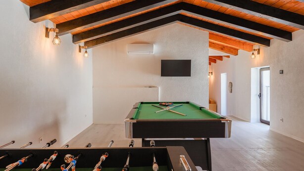 Een kamer met een pooltafel, een tafelvoetbaltafel en een aan de muur bevestigde televisie.