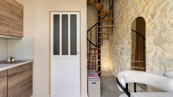 A kitchen with wooden cabinets, a white door with a frosted panel, a staircase with wooden steps, and a stone wall.