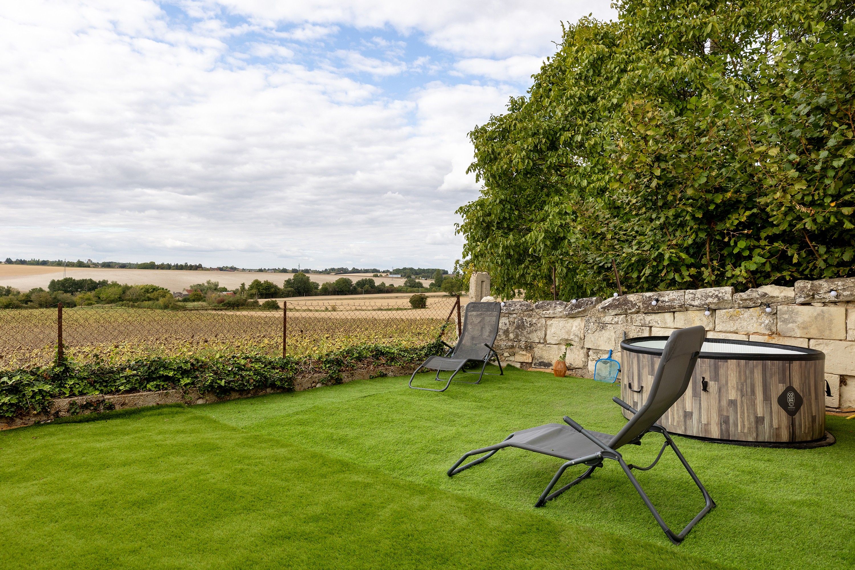 Eine Terrasse mit Blick auf ein Feld, eine Steinmauer und eine Holztonne als Whirlpool.
