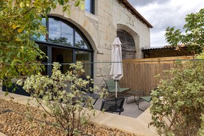 A stone building with a large arched window, a covered patio with a table and chairs, and a bamboo fence. - Holiday Home “Le Pigeonnier Des Châpeaudieres” with Private Terrace, Wi-Fi, Air Conditioning (Châtellerault)