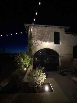 Un edificio de piedra con un amplio acceso en arco y un garaje. Hay luces colgantes sobre la entrada y una pequeña ventana en la pared superior.