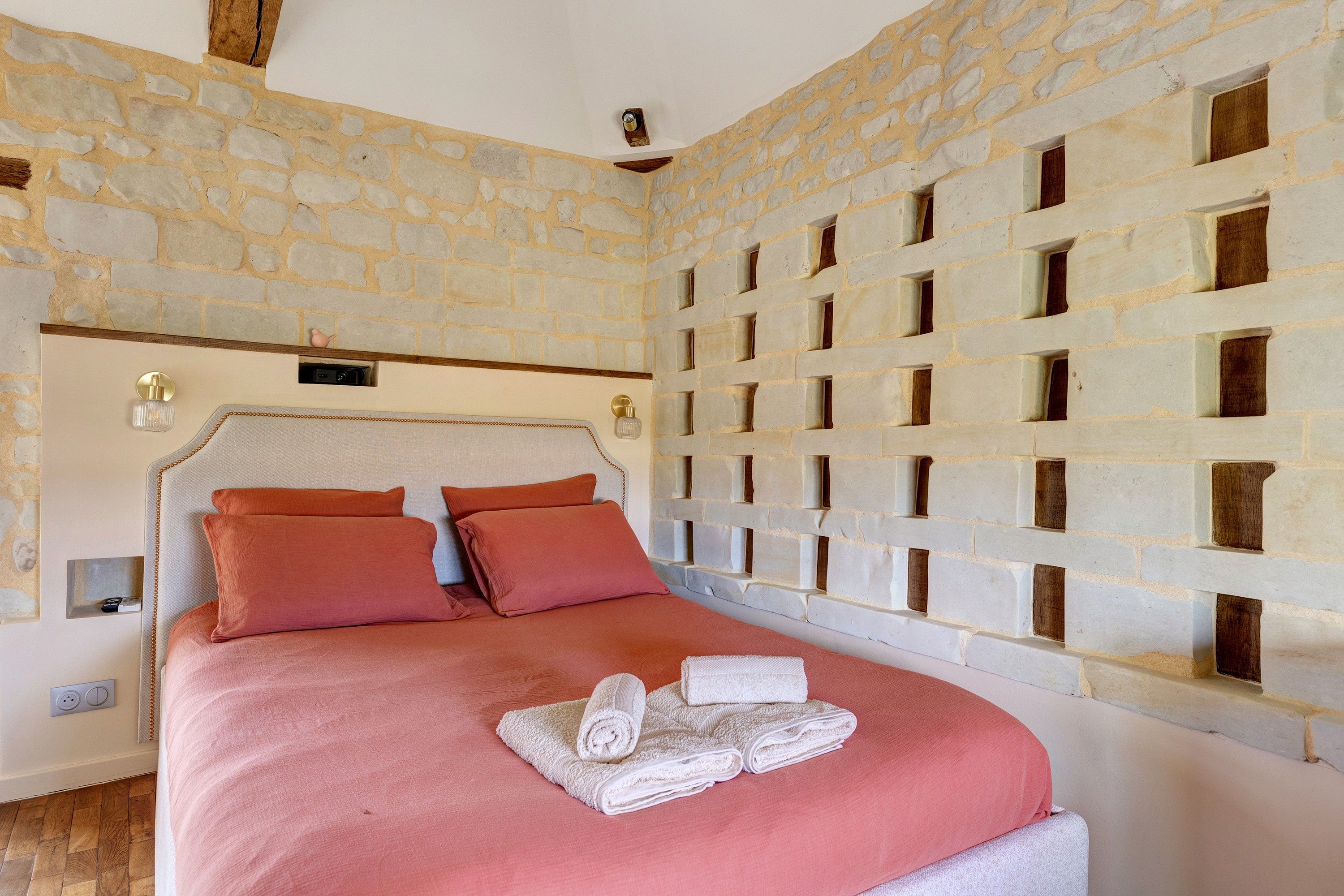 A bedroom with a stone wall, a bed with pink bedding, and a towel on the bed.