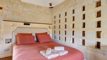 A bedroom with a stone wall, a bed with pink bedding, and a towel on the bed.