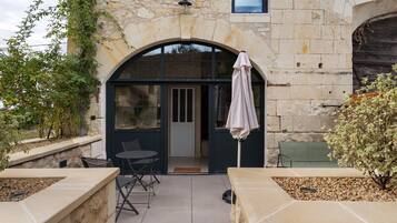 A stone building with a patio area featuring a table and chairs, a covered seating area, and a view through a large window.