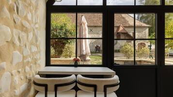 A room with a stone wall, a window with a view of a garden, and a small table with a vase.