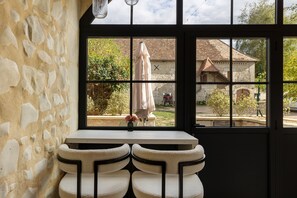 Une pièce avec un mur en pierre, une fenêtre donnant sur un jardin et une petite table sur laquelle est posé un vase.