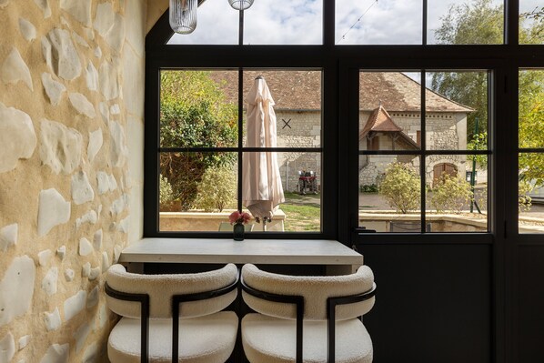 A room with a stone wall, a window with a view of a garden, and a small table with a vase.