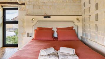 Un dormitorio con pared de piedra, una cama con dos almohadas y una ventana con vistas a edificios.
