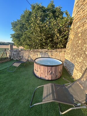 Un jacuzzi con revestimiento de madera, rodeado por un muro de piedra y un césped.