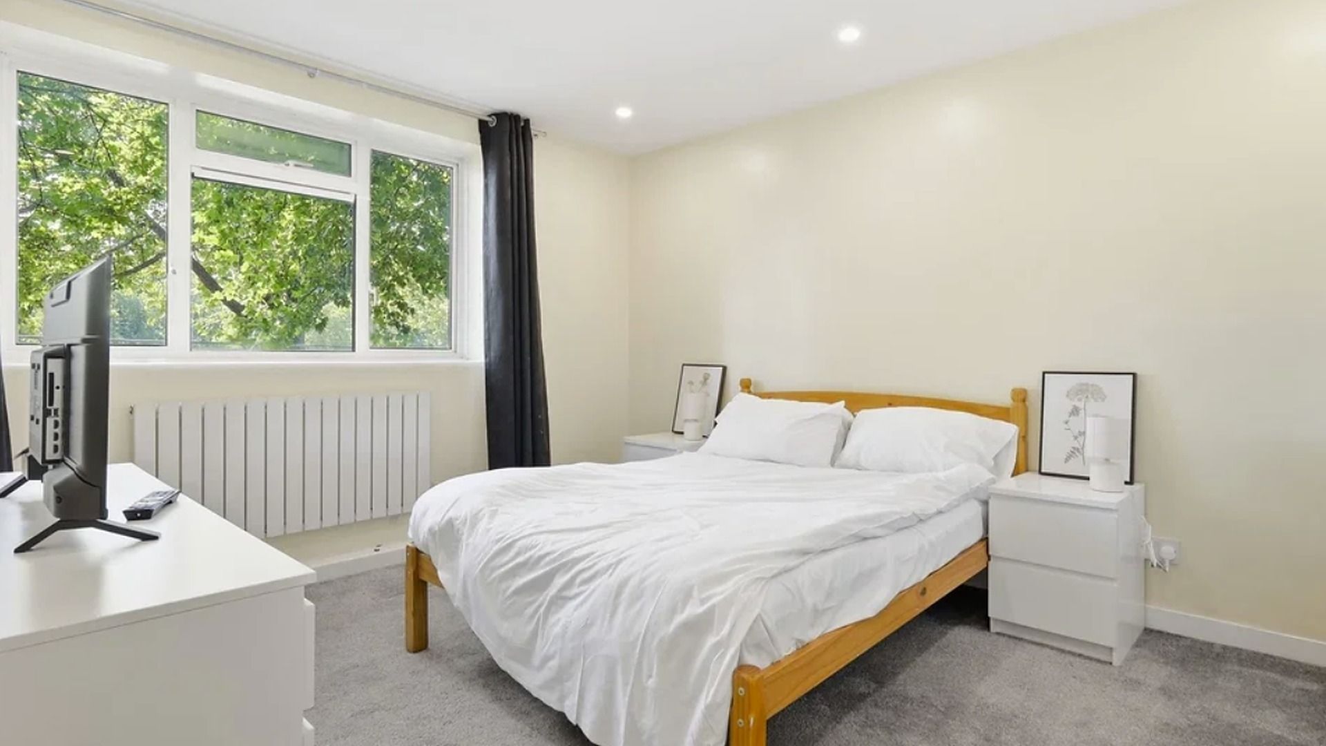 Ein Schlafzimmer mit einem Bett, Nachttischen, einem Schreibtisch mit Computer und einem Fenster mit Vorhängen.