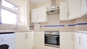 Een keuken met witte kastjes, een roestvrijstalen oven, een wasmachine en een raam.