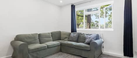 Una sala de estar en esquina con un sofá modular, un ventanal con cortinas y un radiador.