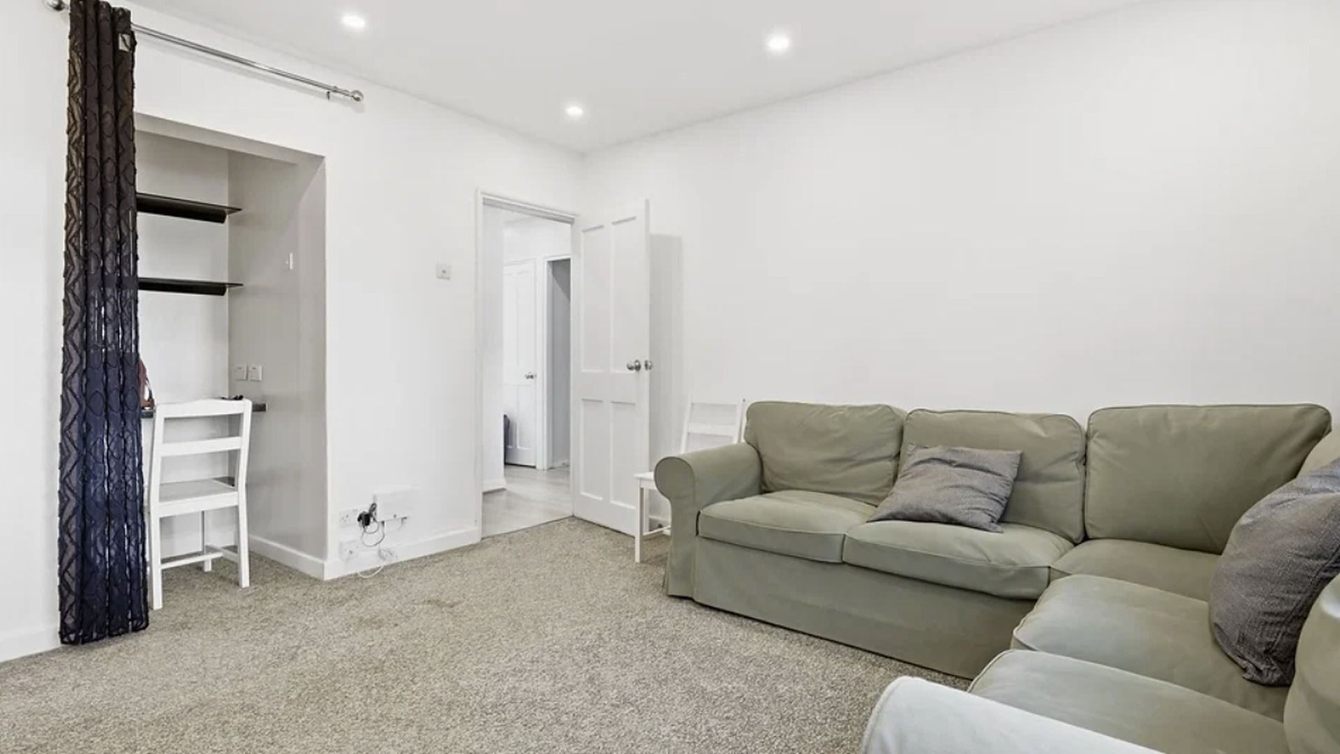 A neutral-toned room with a sofa, a wardrobe, and a door leading to another room.