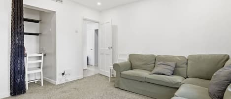 A neutral-toned room with a sofa, a wardrobe, and a door leading to another room.