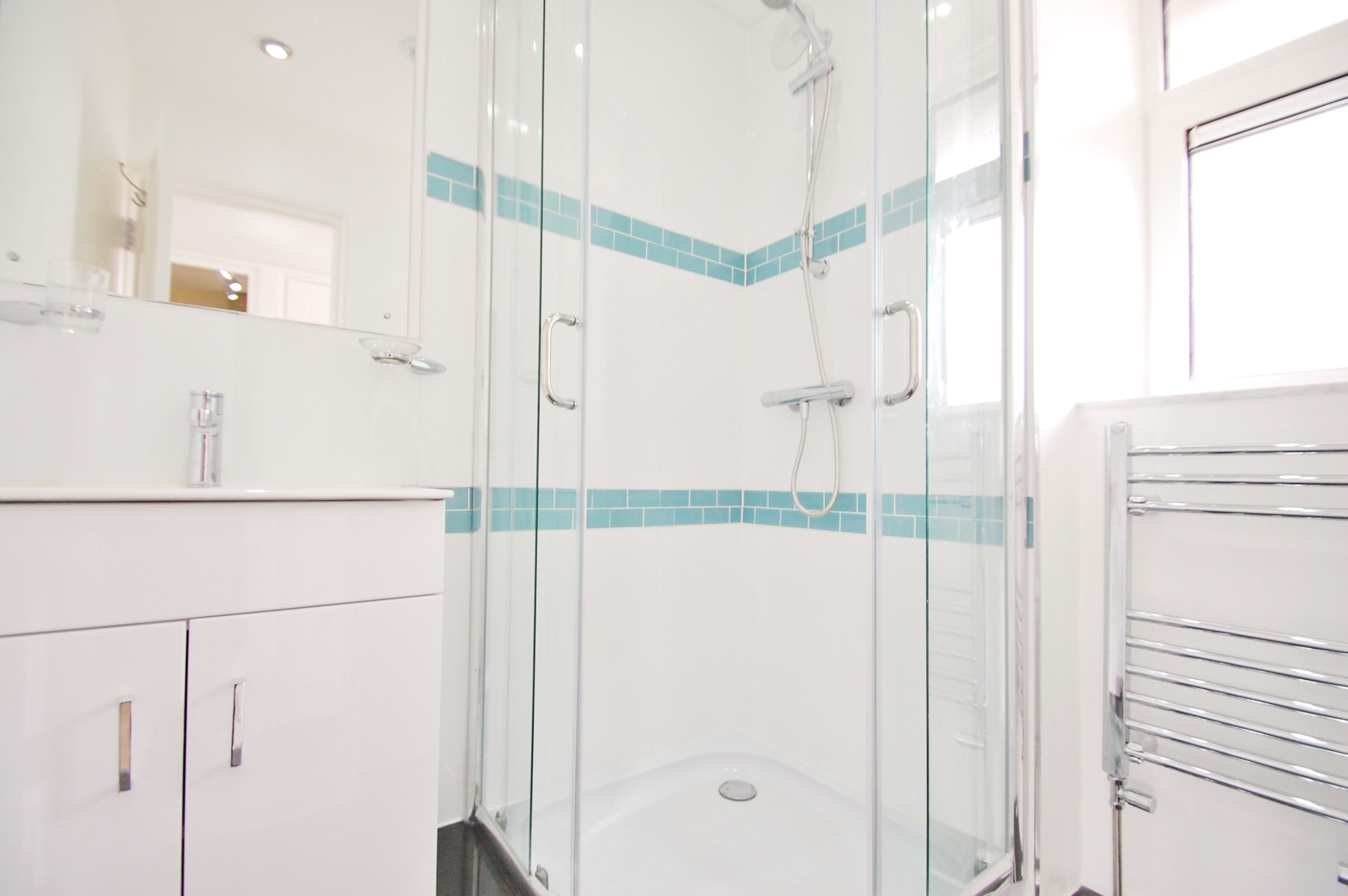 A modern bathroom with a glass-enclosed shower, white cabinetry, and a blue-tiled accent wall.
